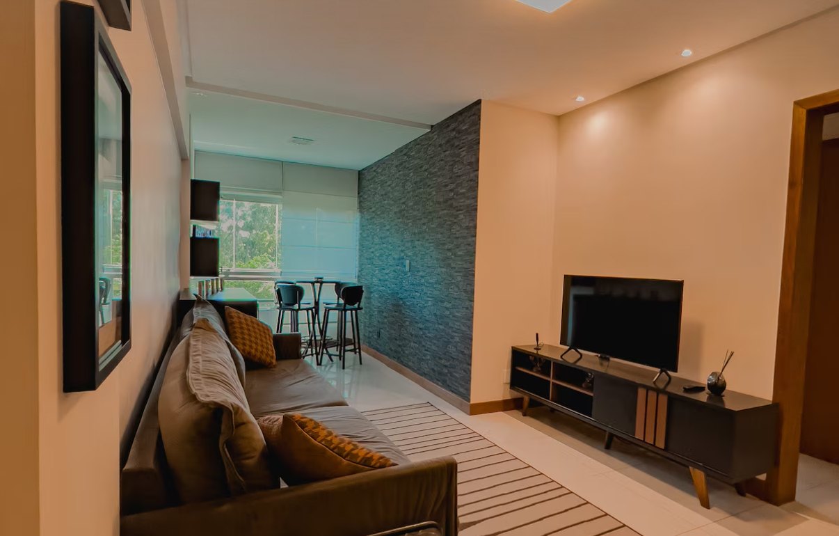 Sala moderna com sofá marrom, parede de pedra, televisão e mesa alta perto da janela