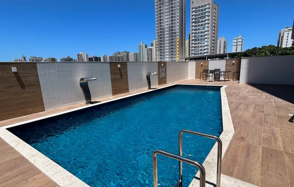 Piscina do condomínio com deck de madeira e prédios ao fundo, em Itaparica